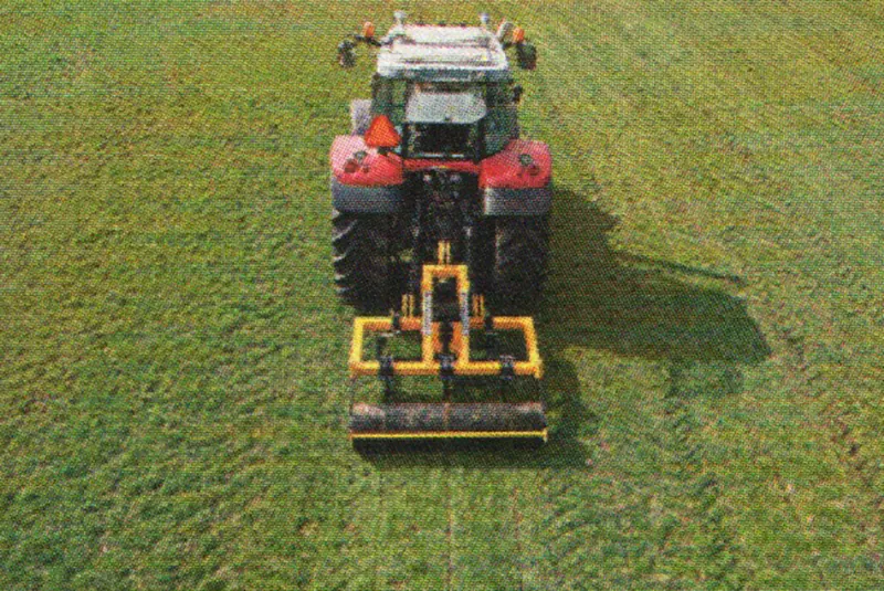 Roter Traktor mit gelbem Anbaugerät zum Auflockern auf einer Grünlandfläche, von oben fotografiert.