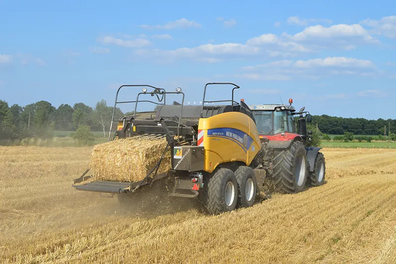 Quaderballenpresse von New Holland hinter einem Traktor auf einem Stoppelfeld, ein Strohballen kommt gerade heraus.